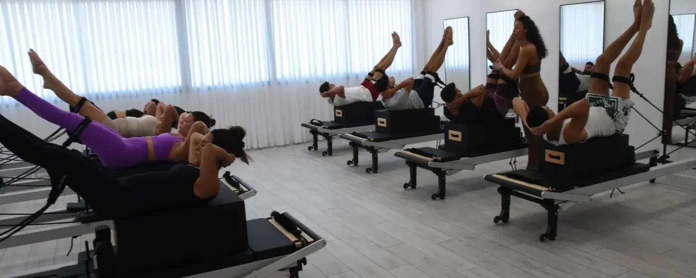שיעור קבוצתי על מכשירי הרפורמר, המתאמנים שוכבים על הקוביות ורגליהם מורמות